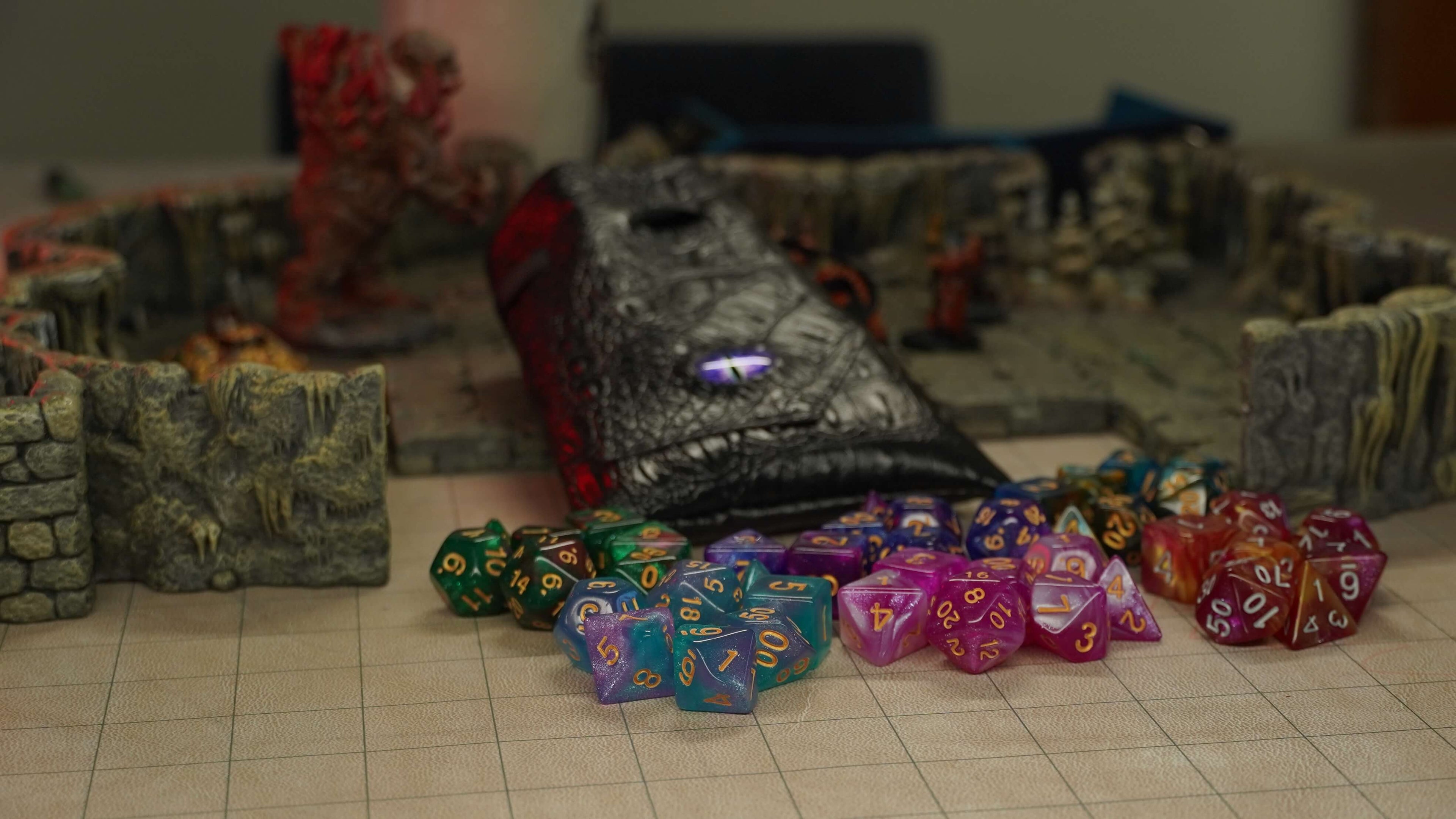 Only Crits Homepage Banner of assorted colorful dice sets from the 'Dragon Eye - Multiple Dice Sets' product scattered around a dungeon battle map with miniatures and a black faux dragon-leather dice bag.