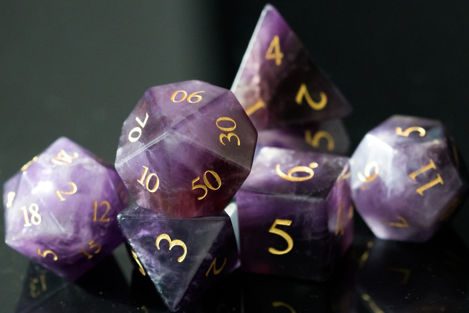 Full 7-piece amethyst gemstone dice set with rich purple hues and gold numbering, displayed on a black reflective surface.