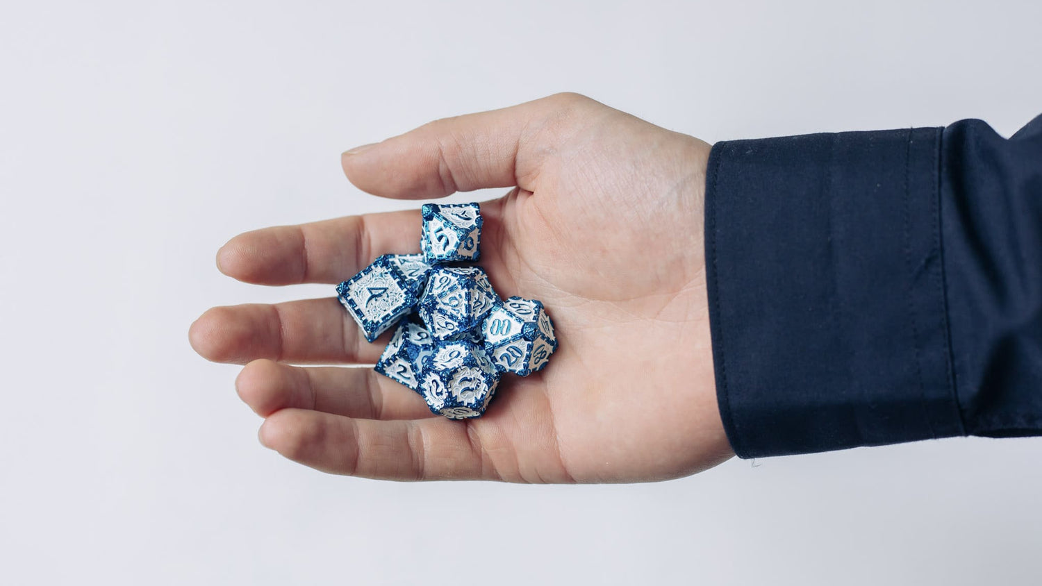 Hand holding a 7-piece blue and white metal dice set for Dungeons & Dragons and other TTRPGs.