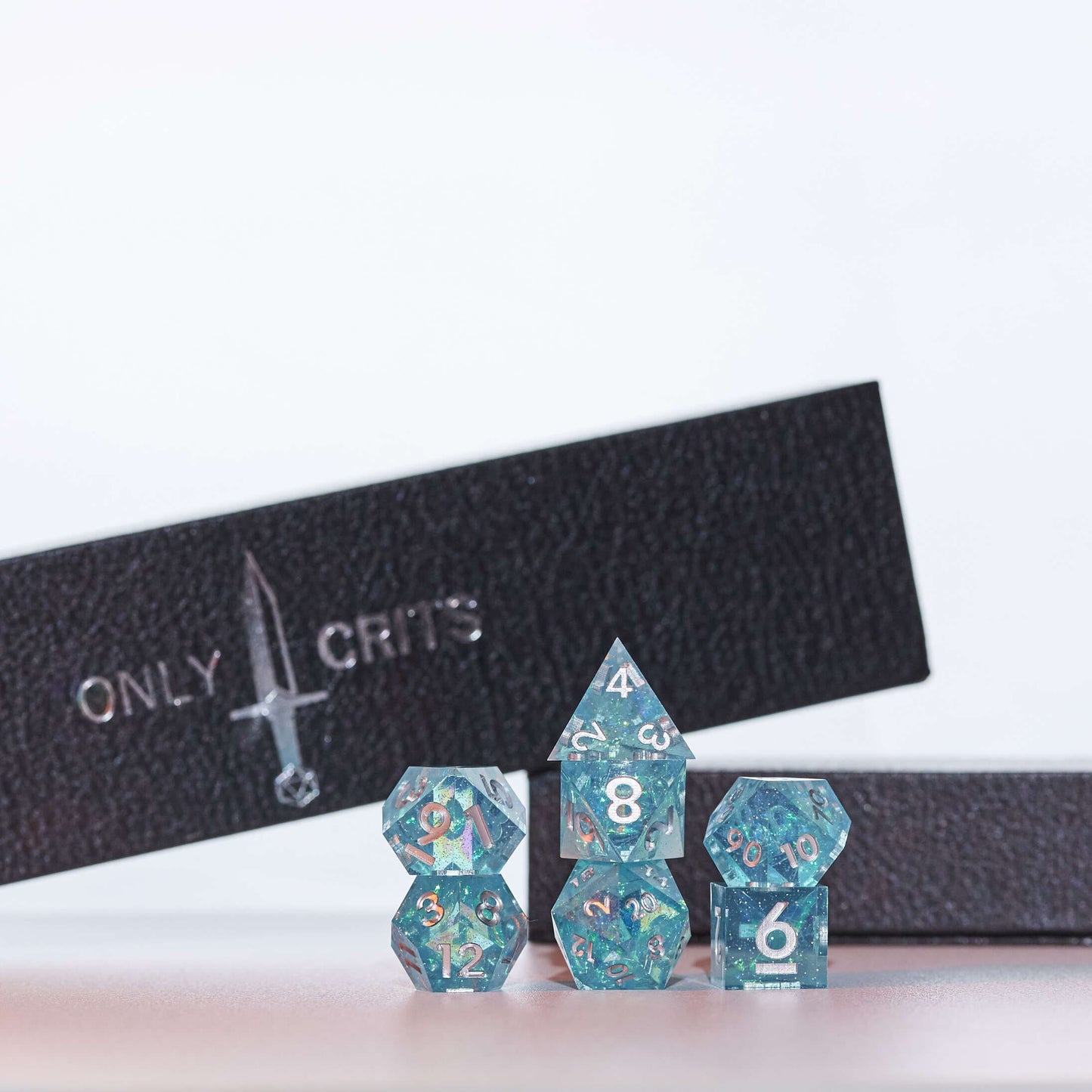 Icy Shard dice set stacked for display with Only Crits box, teal resin dice with silver numbering
