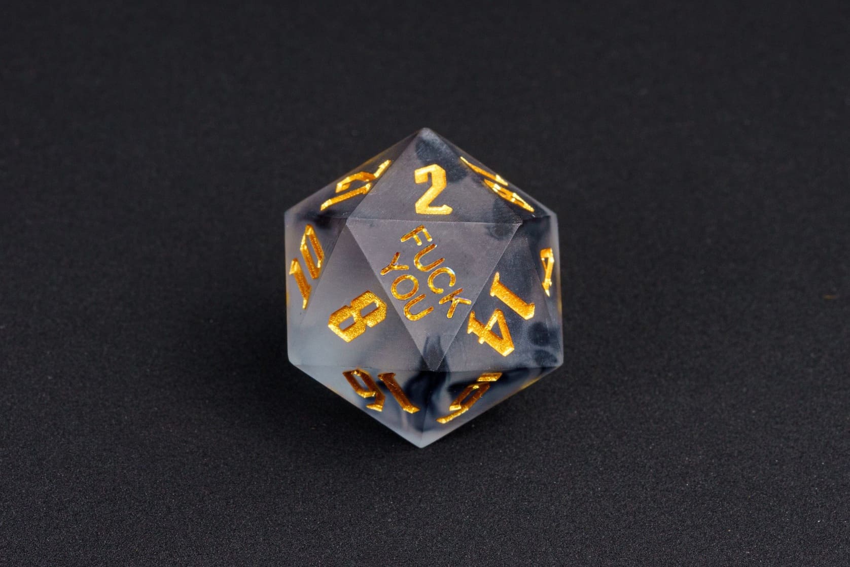 Nimbus Noir sharp-edge D20 from the Fck Me Dice Set, smoky black translucent resin with gold numbering and 'Fck You' lettering