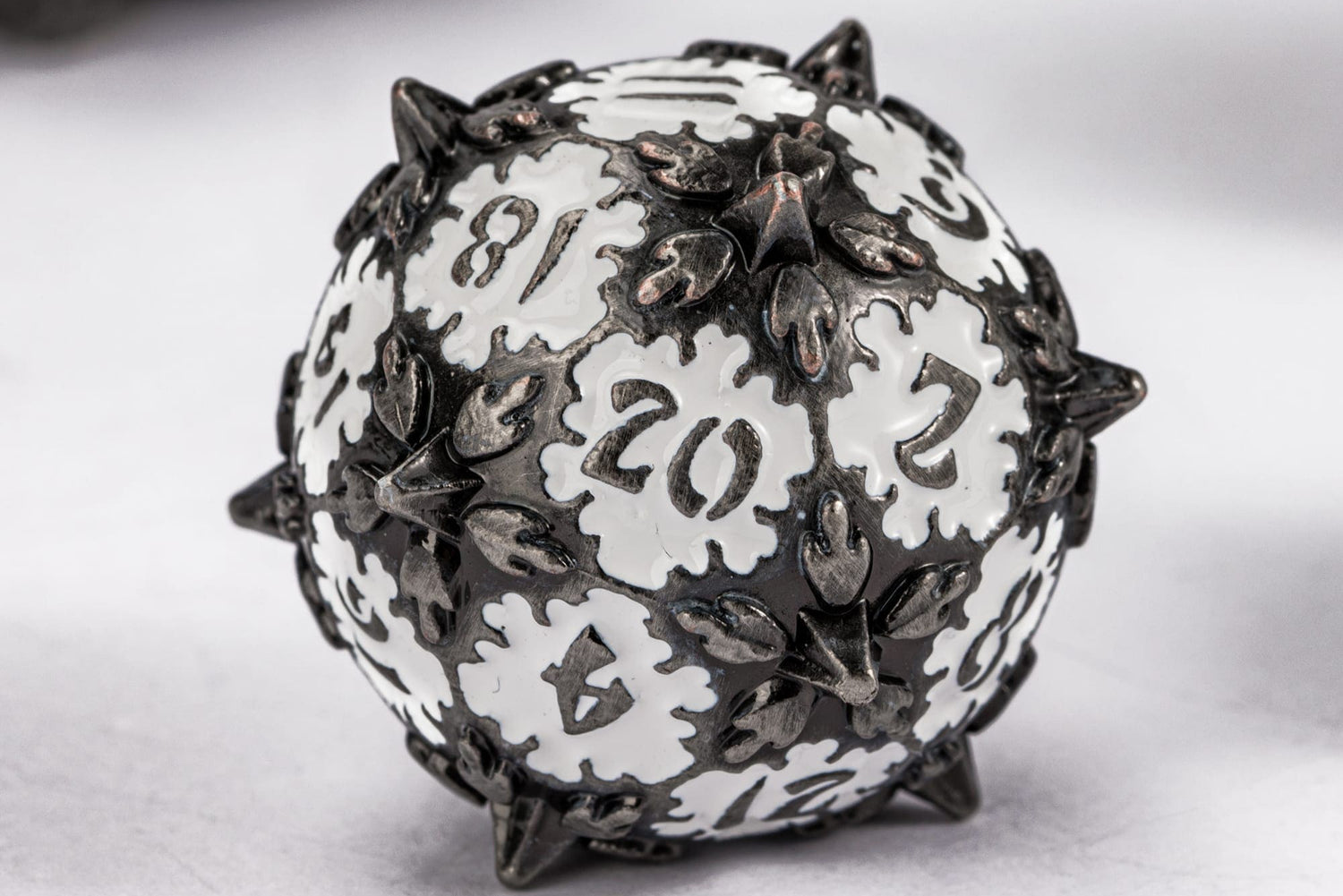 Close-up of spiked white and black metal D20 with intricate gothic design for tabletop RPGs.