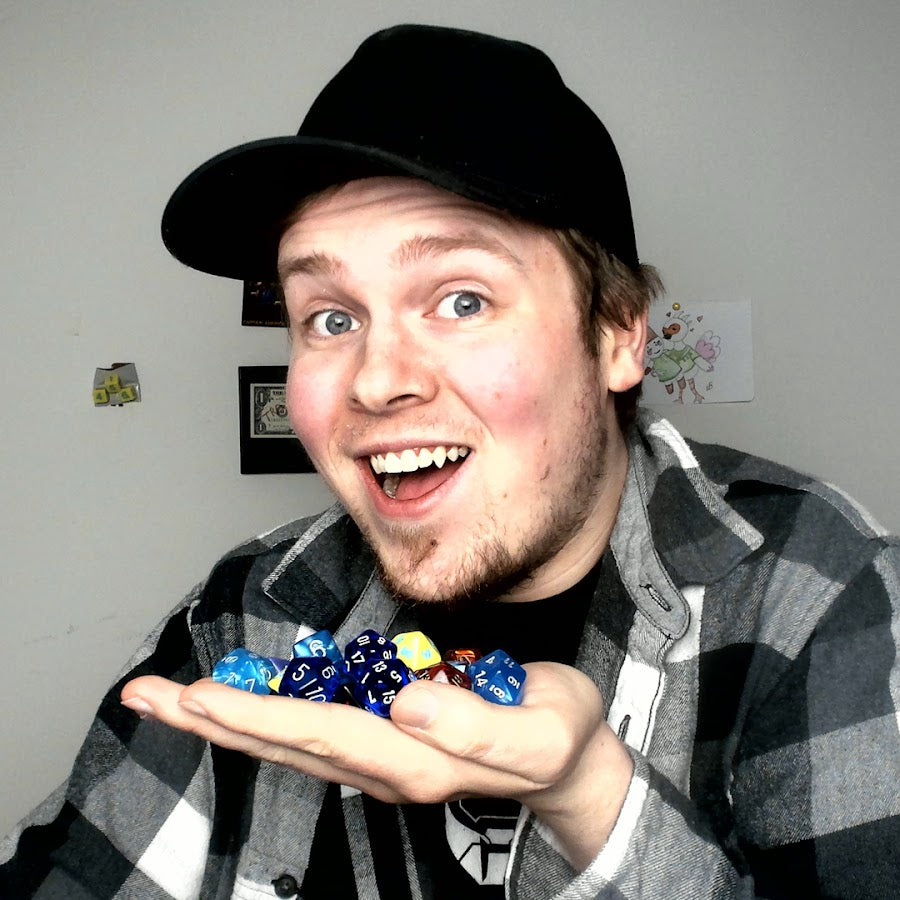 NoNat1s smiling while holding colorful D&D dice in his hand, wearing a black cap and flannel shirt