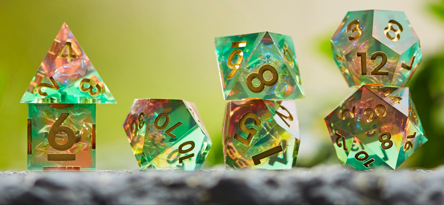 Constellations Essence - sharp edge dice set has green and orange translucent dice with gold numbers, glowing with internal sparkle on stone