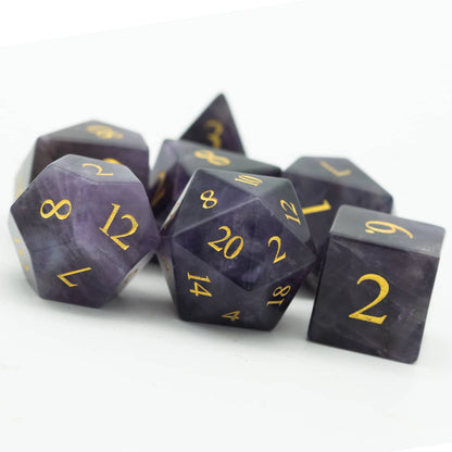 Pile of Amethyst Essence Stone Dice Set with natural purple gemstone finish and gold inking for DnD & RPG play