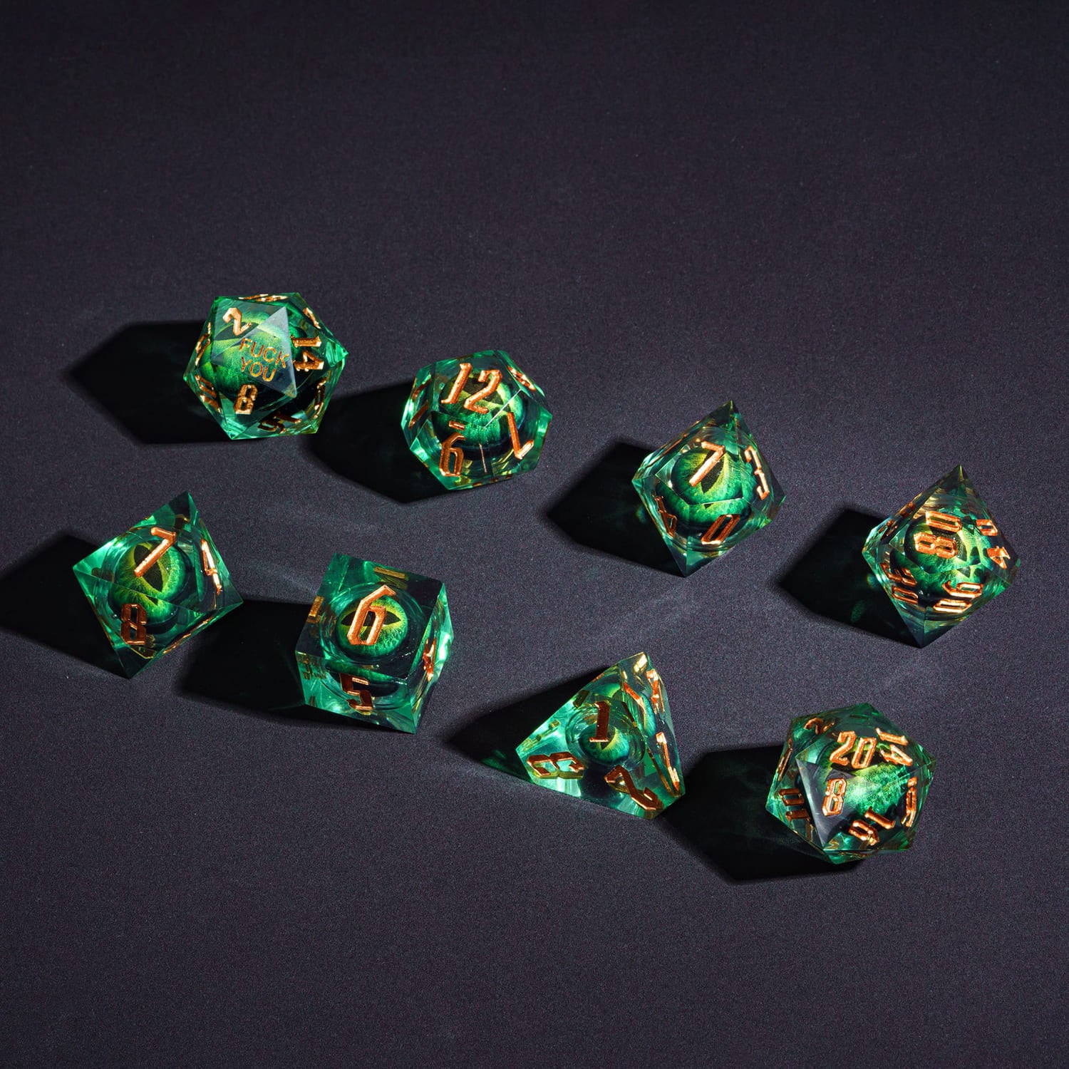 Flat lay of Dragon Eye Green Fck Me Sharp Edge Dice Set 7 piece dice collection with dual D20s Yeet & F*ck