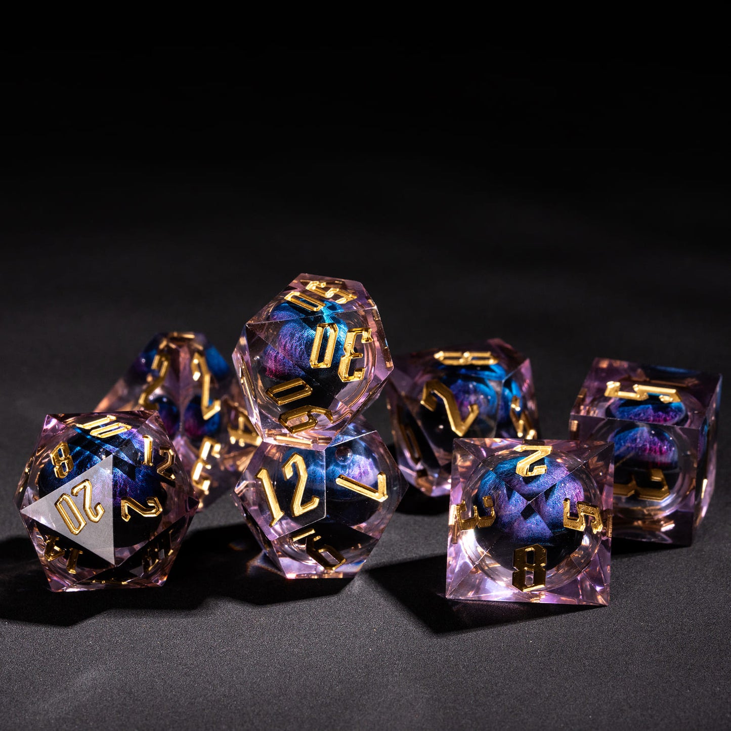 Dragon Eye Purple sharp edge dice set arranged on dark surface showing translucent purple resin and gold numbering