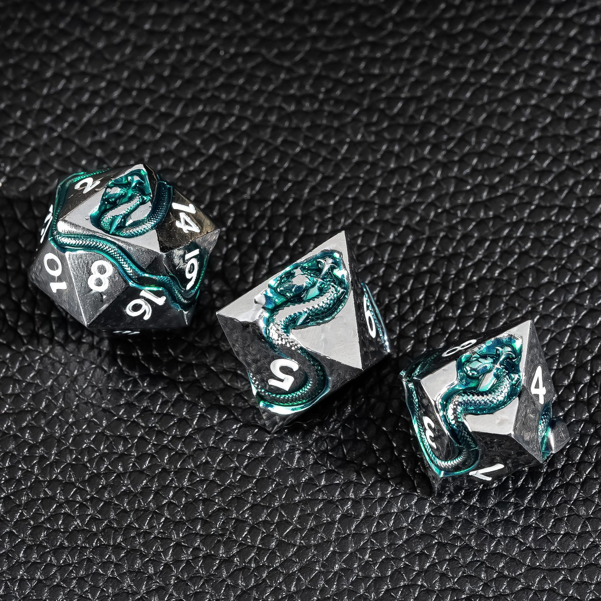 Close up of Emerald Serpent metal dice with green serpent inlay on black textured surface