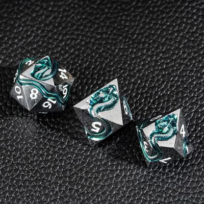 Close up of Emerald Serpent metal dice with green serpent inlay on black textured surface