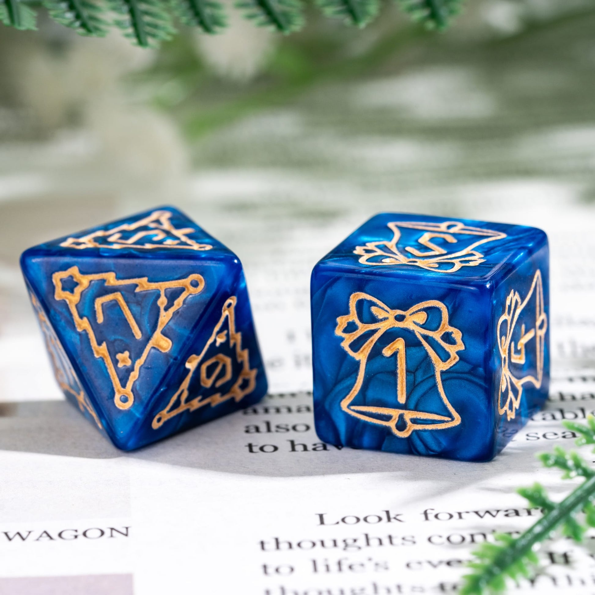 Close up of blue Festive Fate holiday D6 and D8 dice with gold bell and Christmas tree engravings