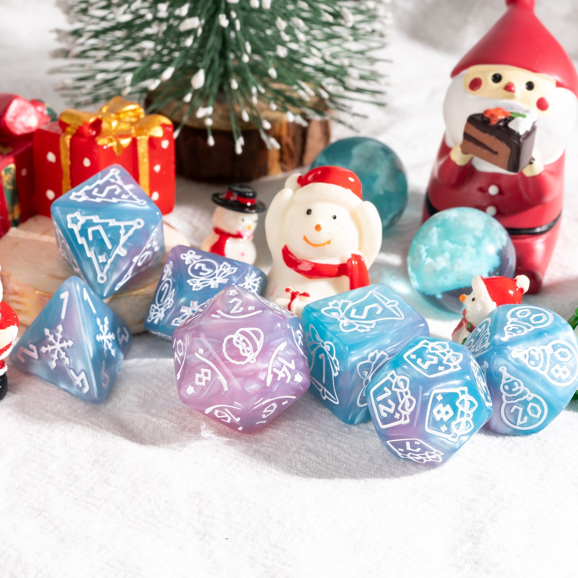 Pink and blue Festive Fate holiday DnD dice set with Christmas themed engravings beside mini snowmen and gifts