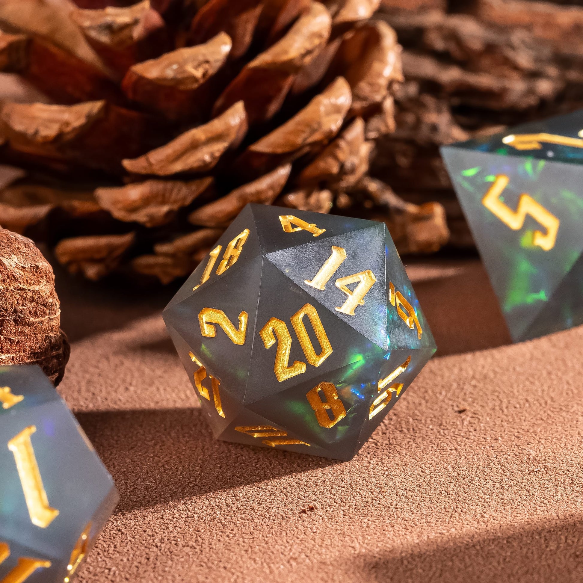 Frosted Mirage sharp edge D20 with gold numbering and green shimmer inclusions beside pinecone