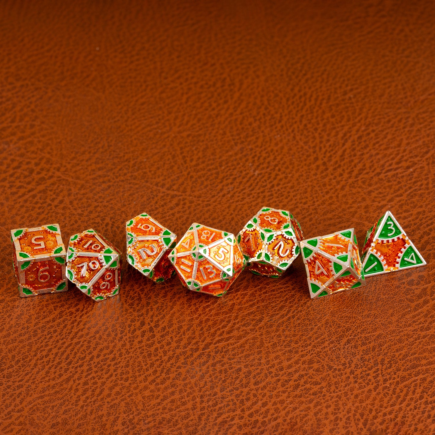 Guillman's Guilded Metal Dice Set arranged in a row on a brown leather surface, displaying all seven polyhedral dice