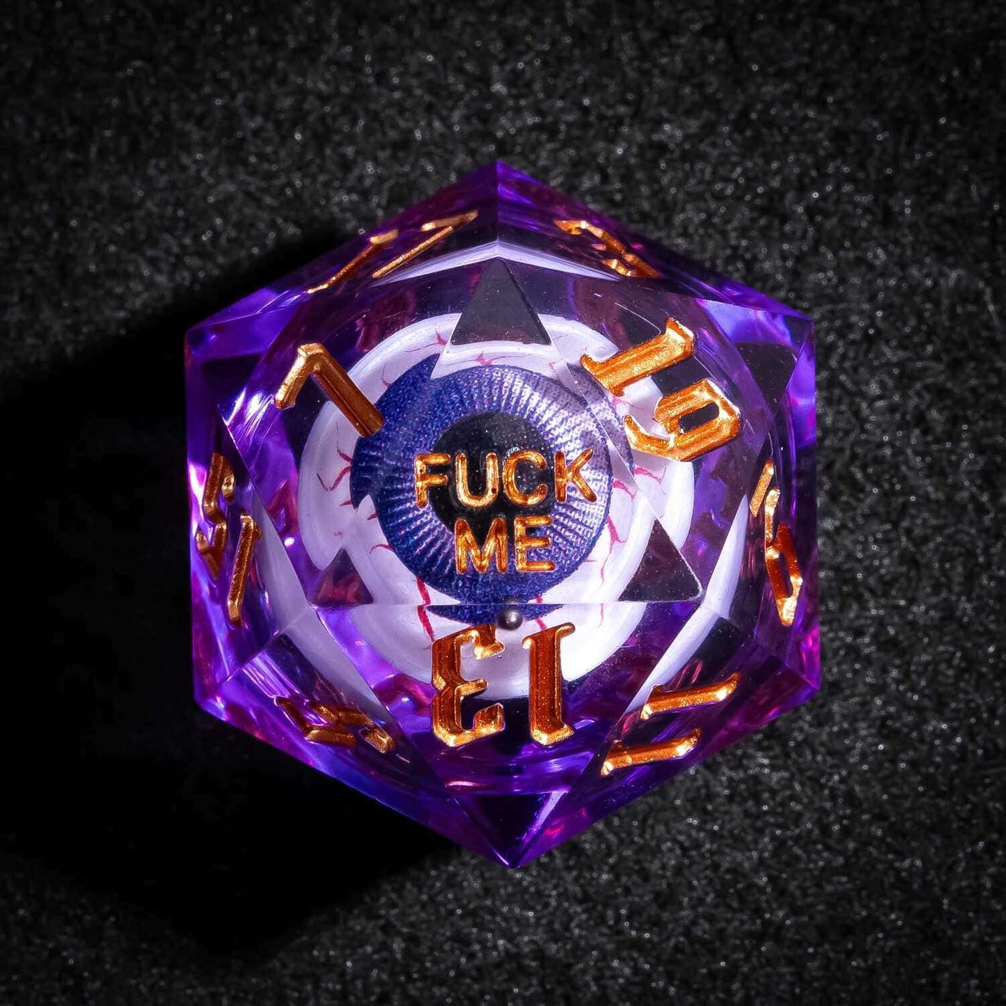 Close up of purple Liquid Core Eyeball D20 with gold numbers and Fuck Me face for tabletop RPGs