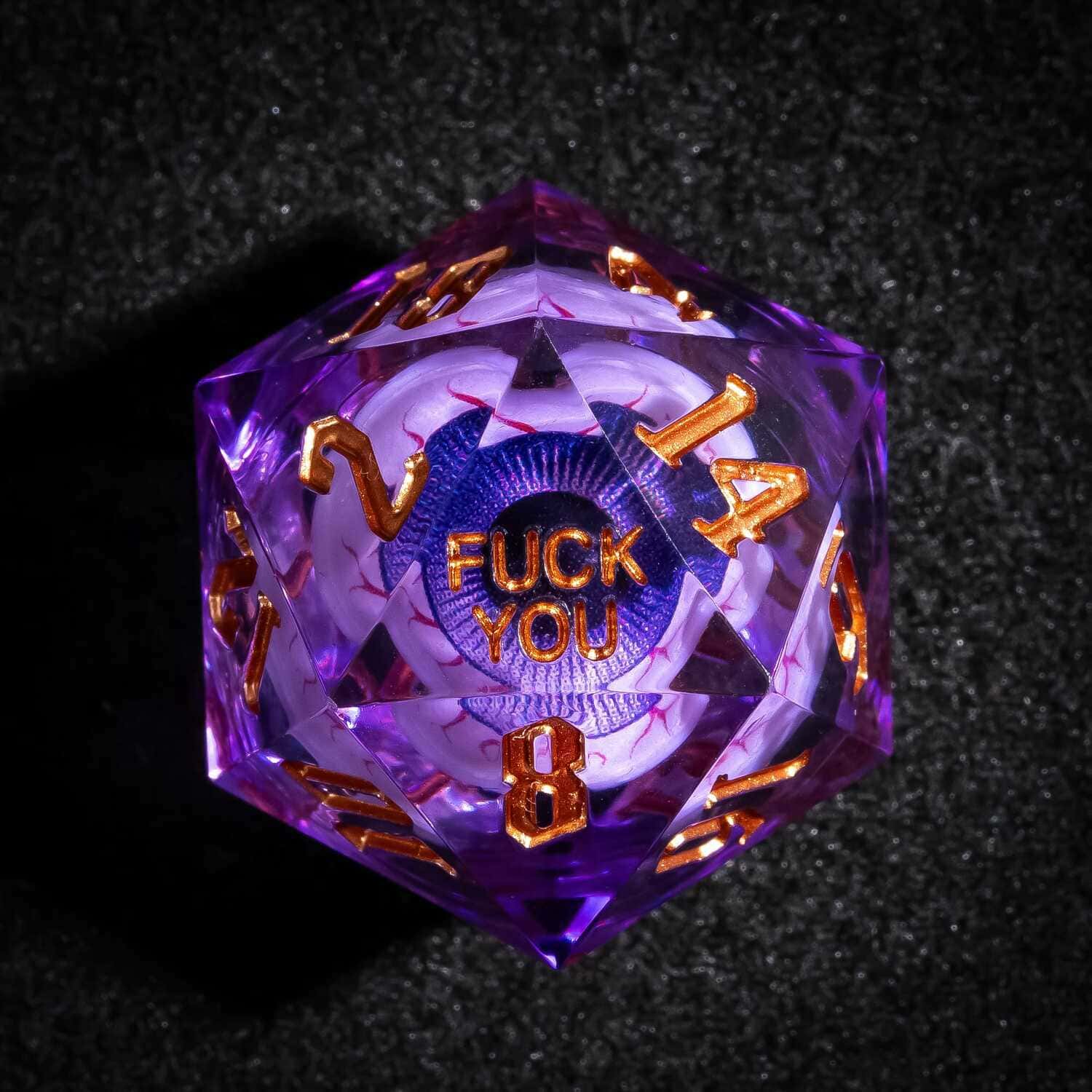 Close up of purple Liquid Core Eyeball D20 with gold numbers and F*ck You face for DnD dice sets