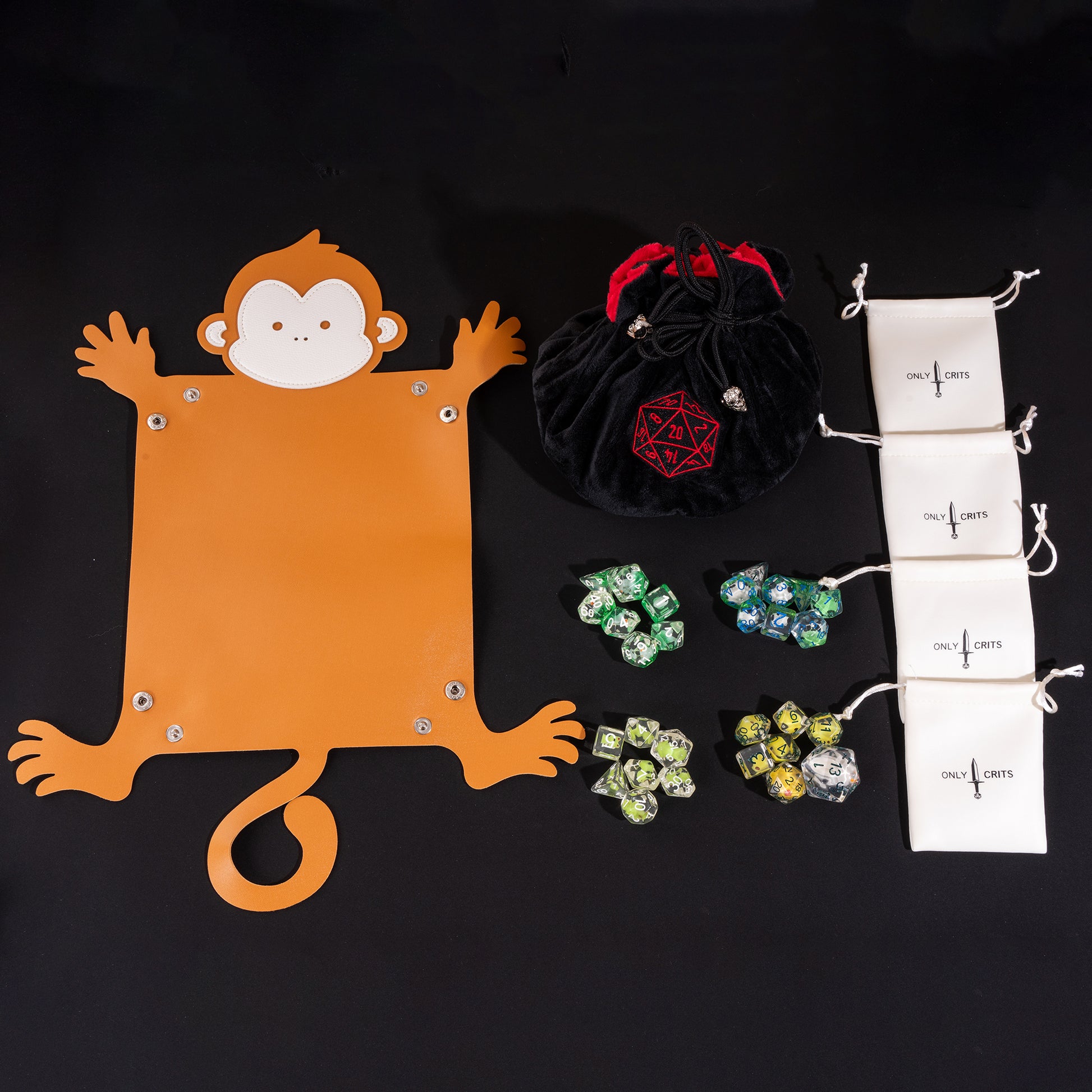 Flat lay of the Little Friends Dice Bundle featuring the monkey-shaped dice tray, premium velvet dice bag, four drawstring dice bags, and four colorful polyhedral dice sets