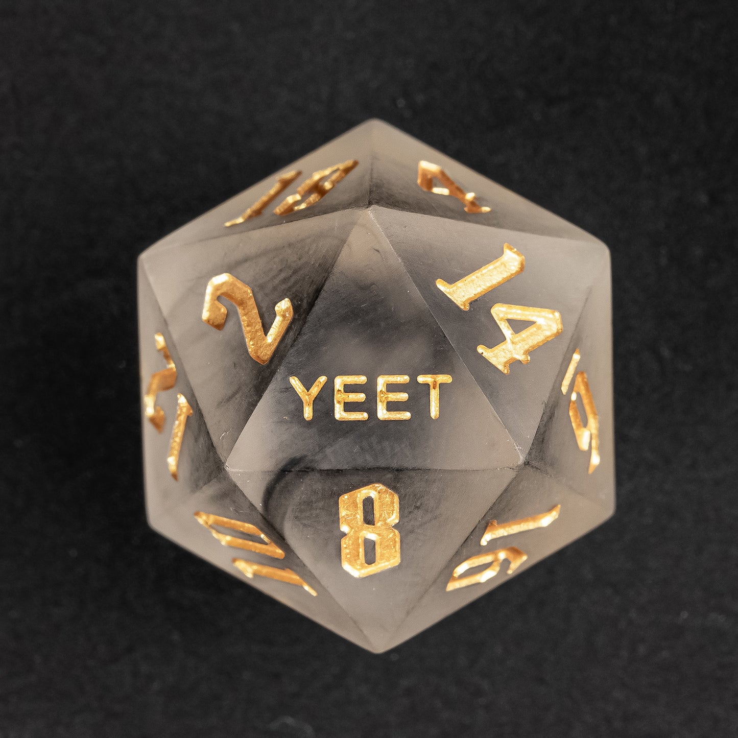 Close-up of Nimbus Noir Yeet Me sharp edge D20 with black smoke resin and gold numbers