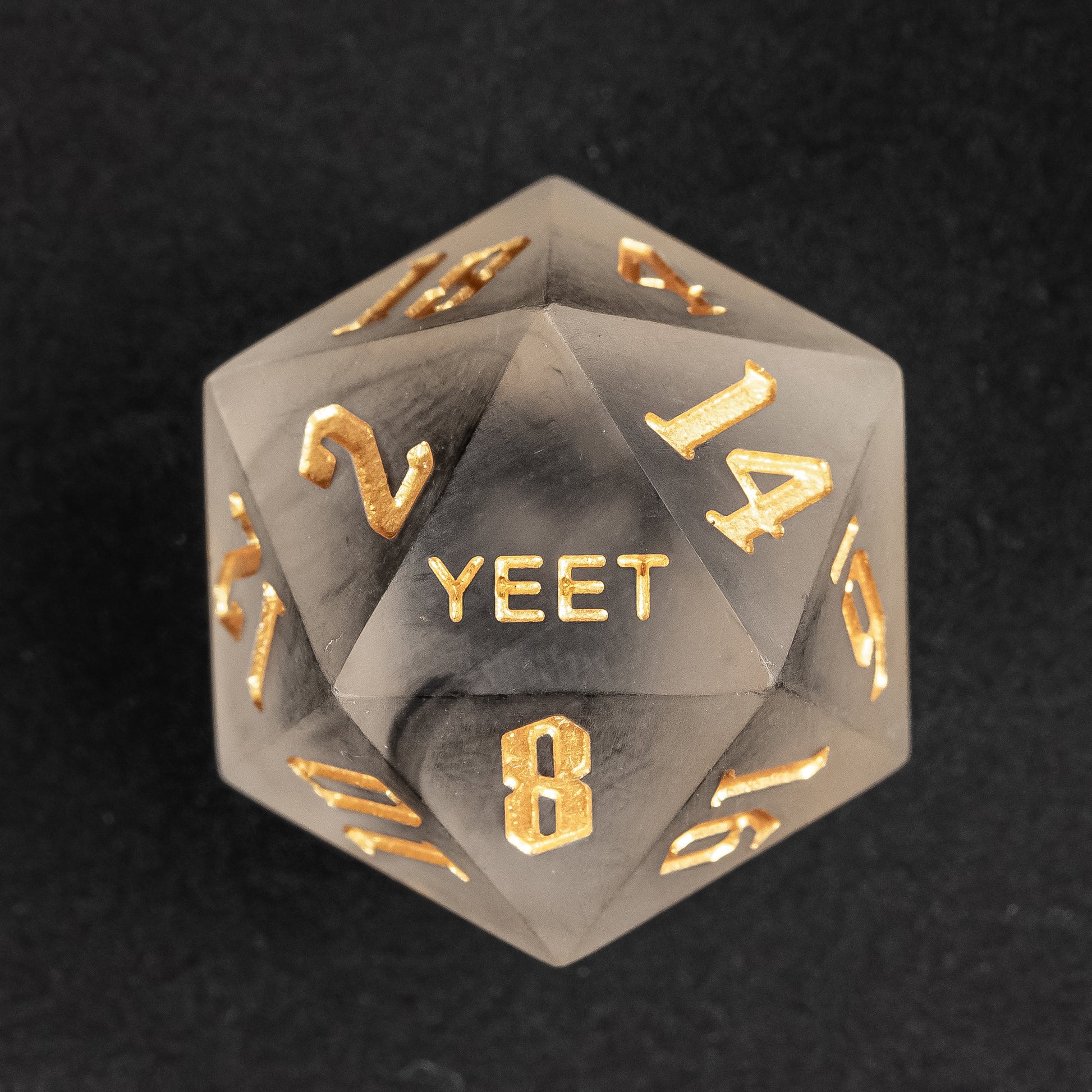 Close-up of Nimbus Noir Yeet Me sharp edge D20 with black smoke resin and gold numbers