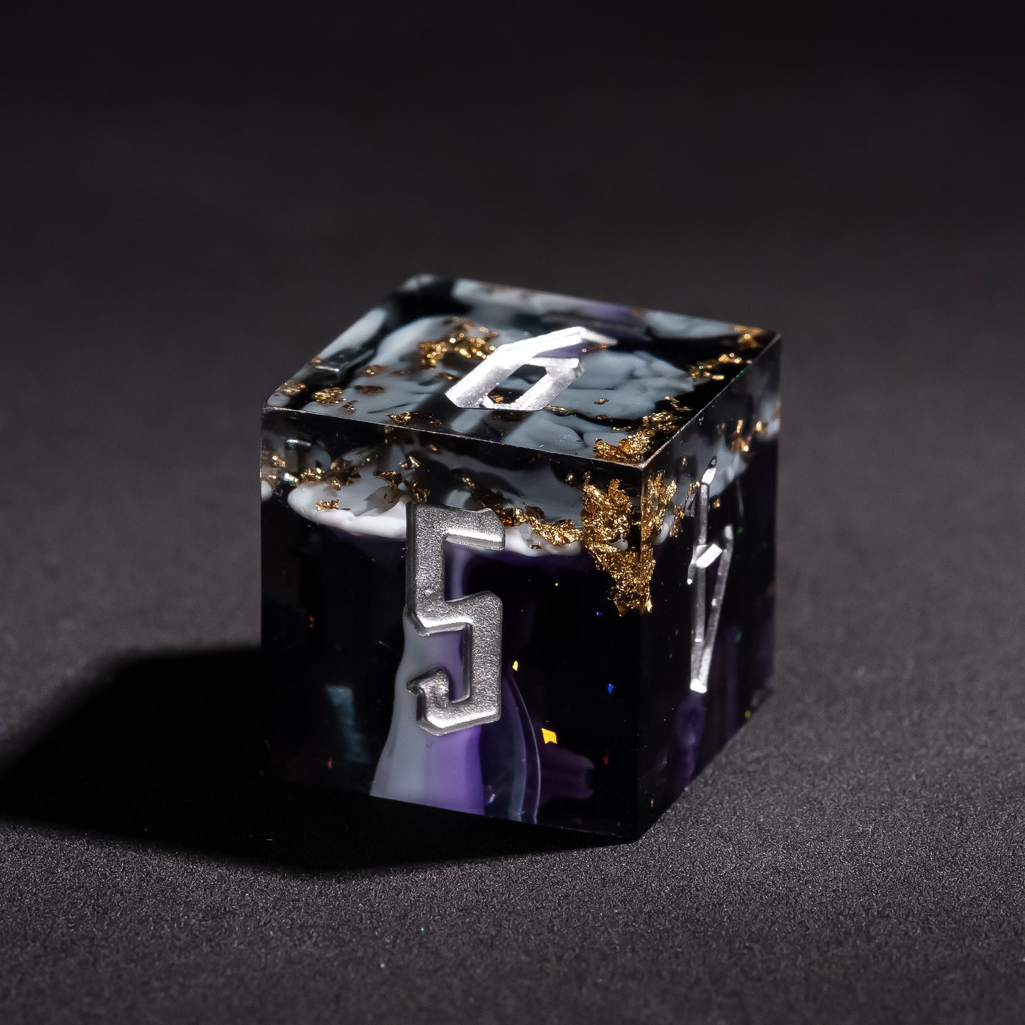Close up of Siren’s Cache D6 sharp edge resin die with gold foil flakes and silver engraved numbering