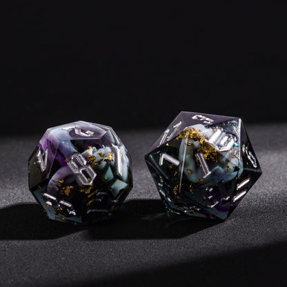 Close up of Siren’s Cache sharp edge D20 and D12 resin dice with gold foil flakes and silver numbering on black background
