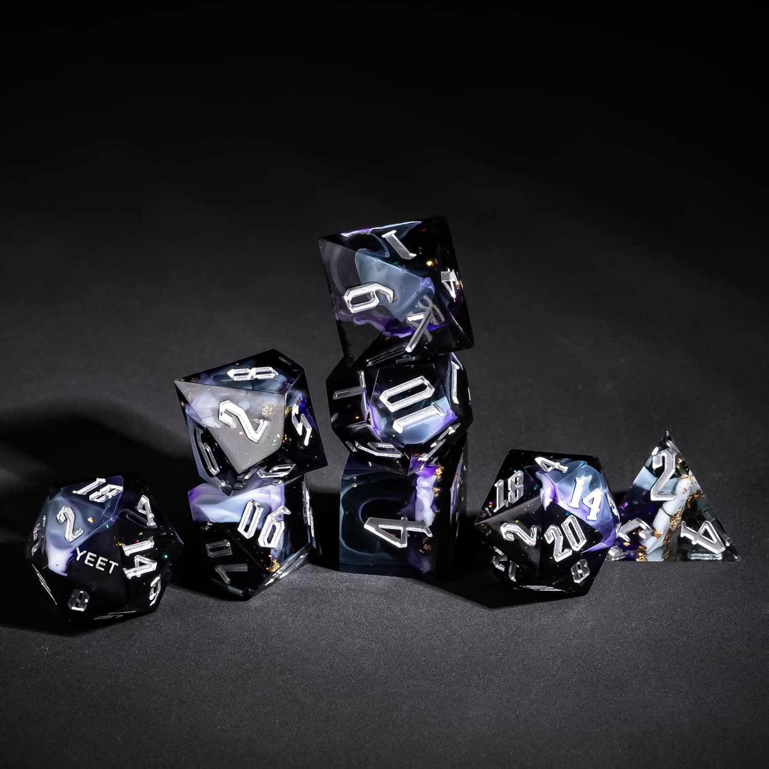 Stacked display of Siren's Cache Yeet Sharp Edge Dice Set with silver numbers