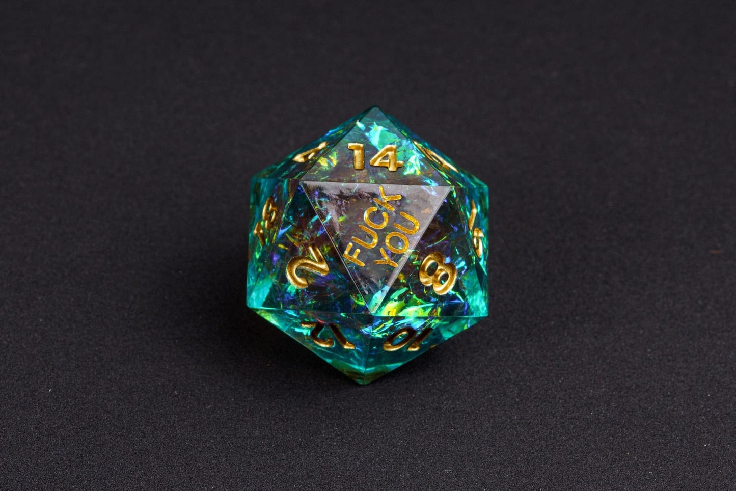 Starlight Nebula sharp-edge D20 from the Fck Me Dice Set, shimmering teal resin with gold numbering and 'Fck You' lettering