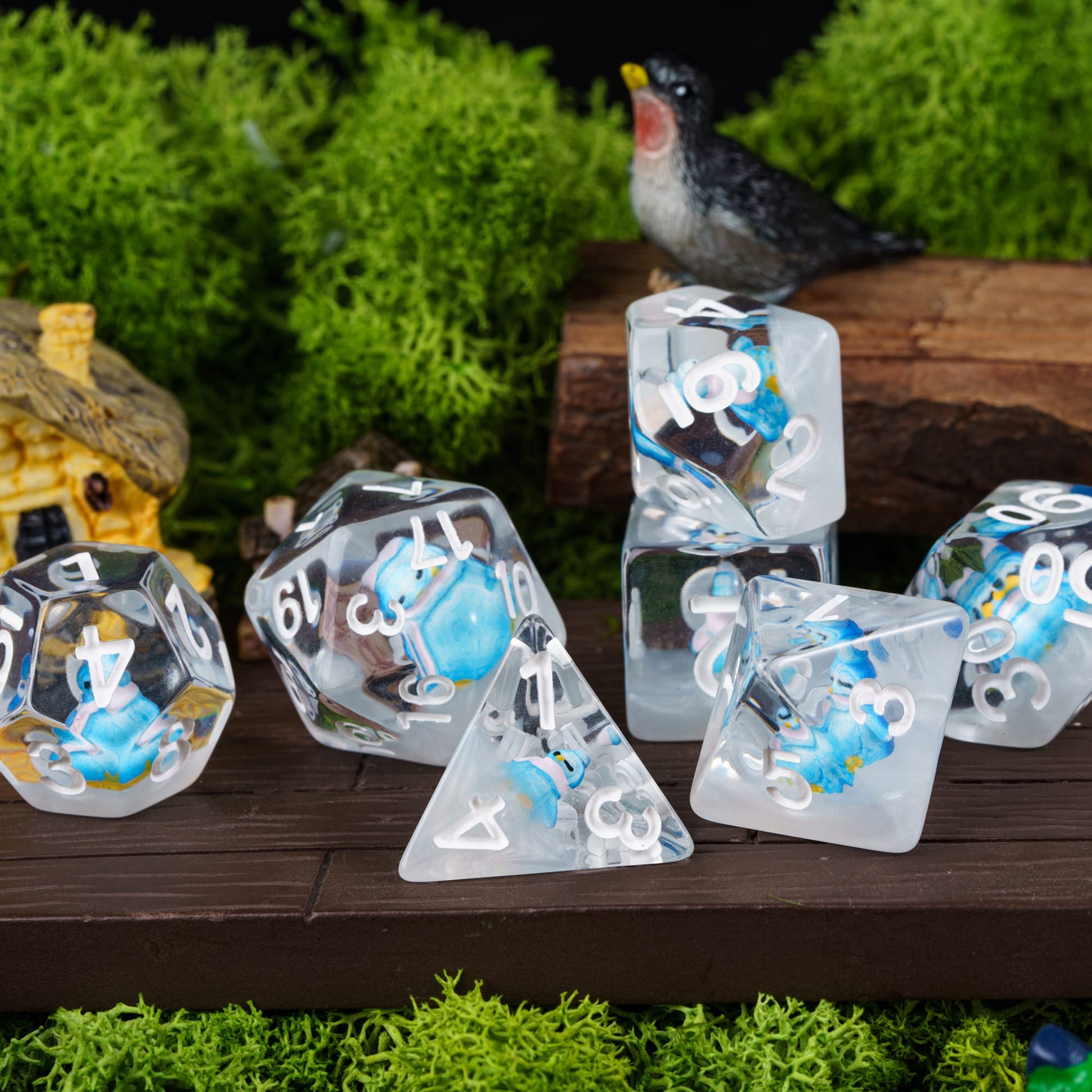 Transparent Blue Penguin dice set arranged outdoors with moss and bird figurine
